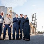 Engineers working at chemical plant standing in front of storage tanks.